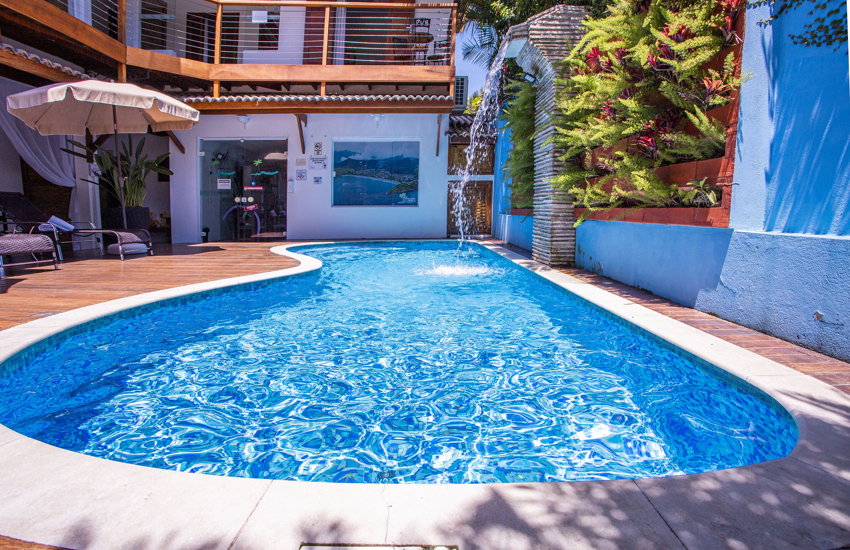A swimming pool with a wooden deck, lounge chairs, and a covered area with an umbrella.
