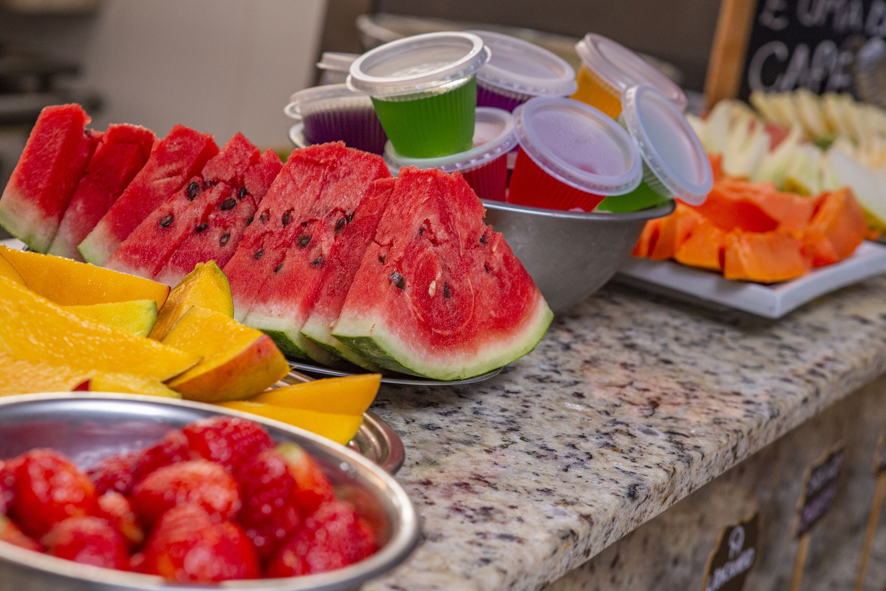 A variety of fresh fruits including watermelon, mango, and strawberries displayed on a granite countertop.