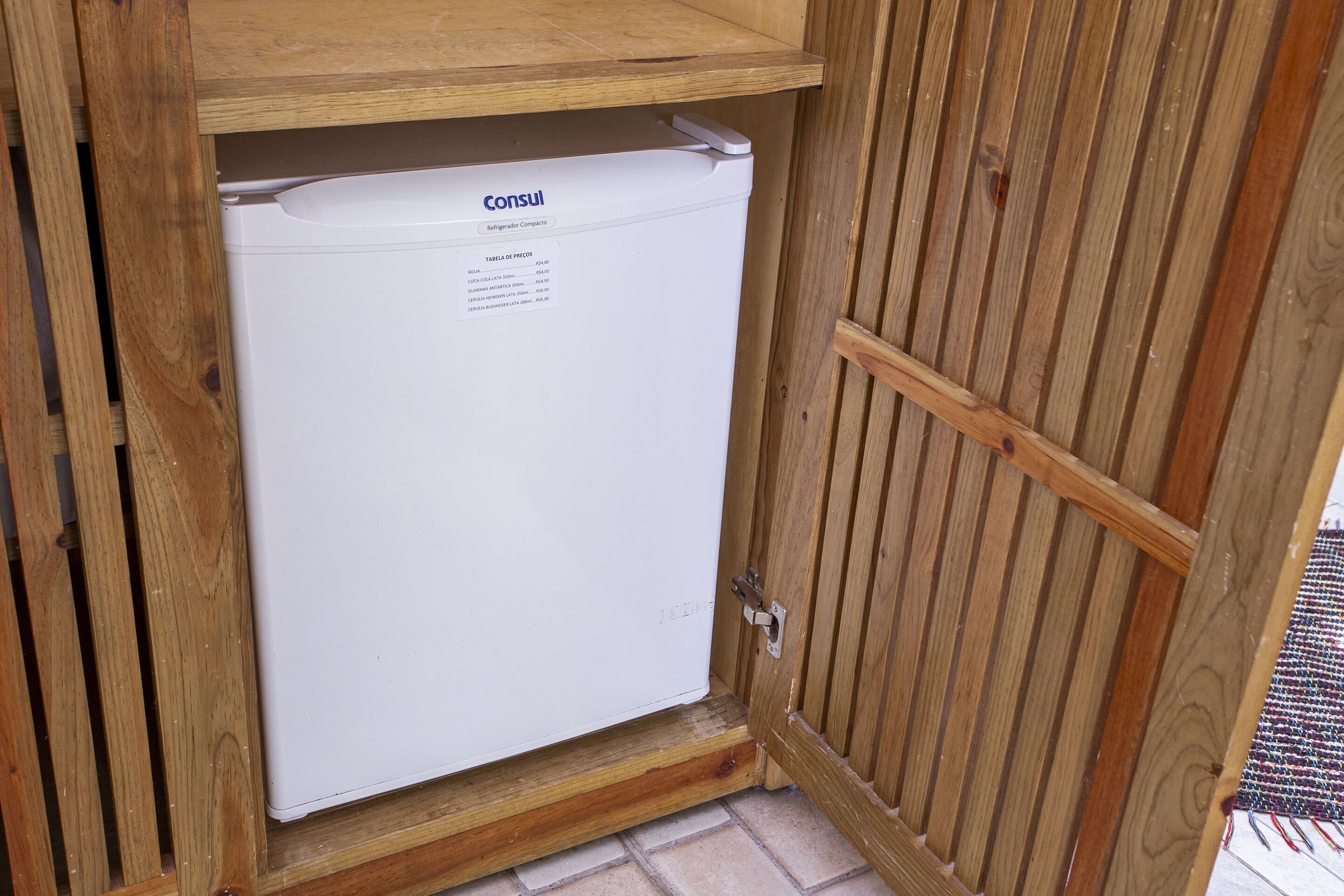 A white refrigerator with a label, placed under a wooden cabinet.