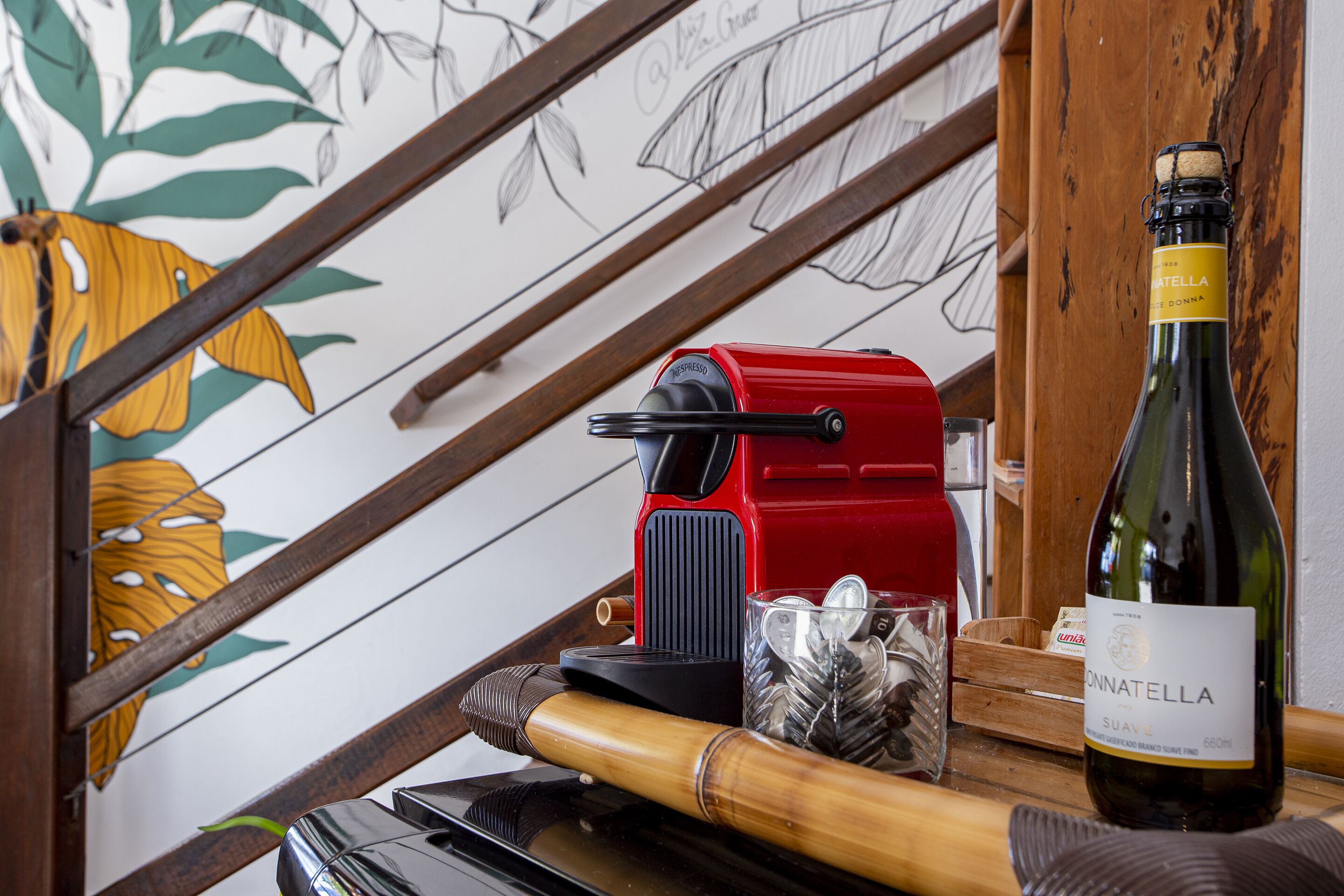 Un escalier en bois, un appareil électroménager rouge, une bouteille de vin et un verre rempli de glaçons, le tout posé sur une table en bois.