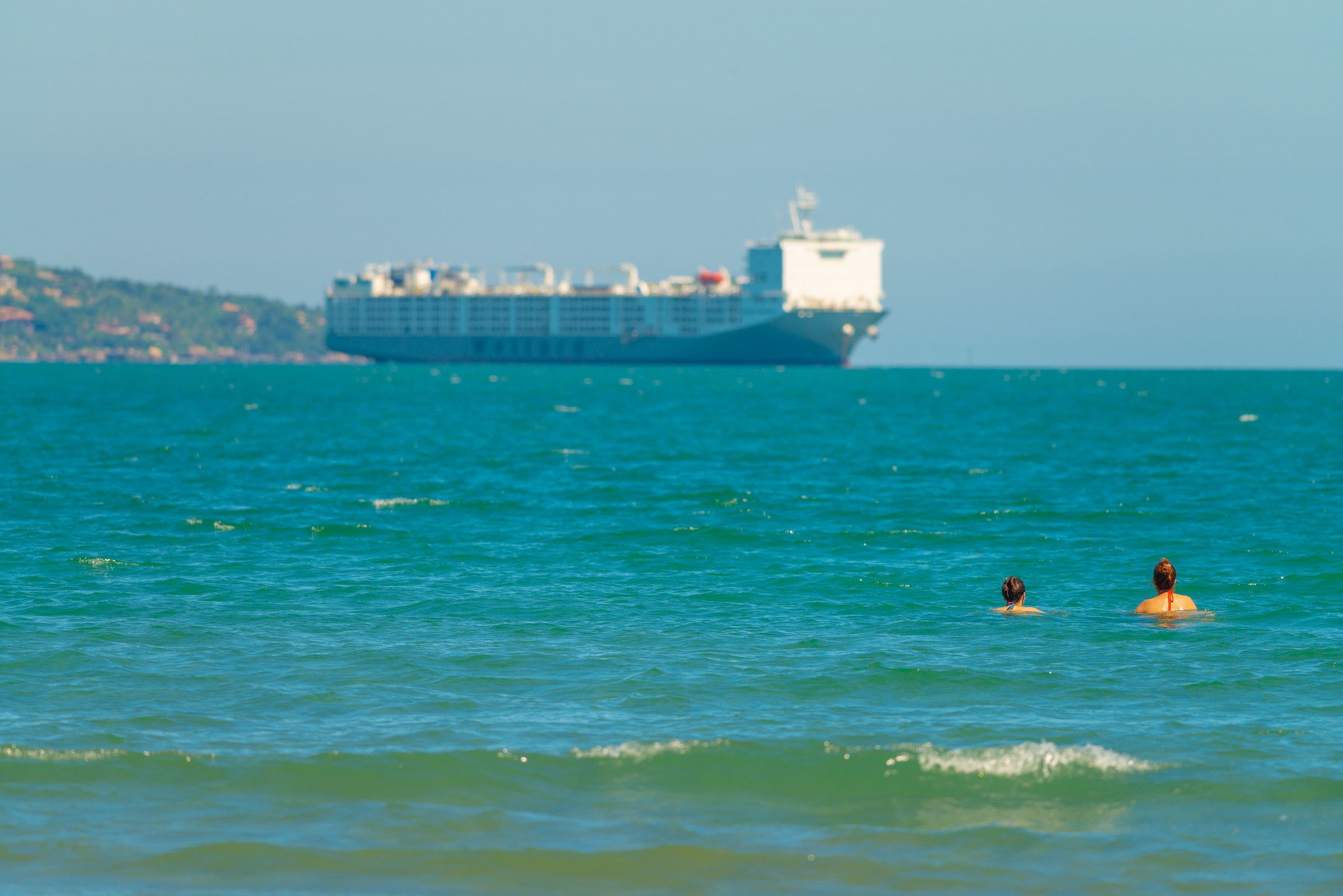 Un gran barco en el océano con dos personas nadando en el agua.