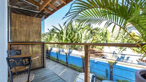 A wooden deck with a table and chairs, a blue wall, and a view of palm trees and a car in the background. - Pousada Vila Barequeçaba (São Sebastião)