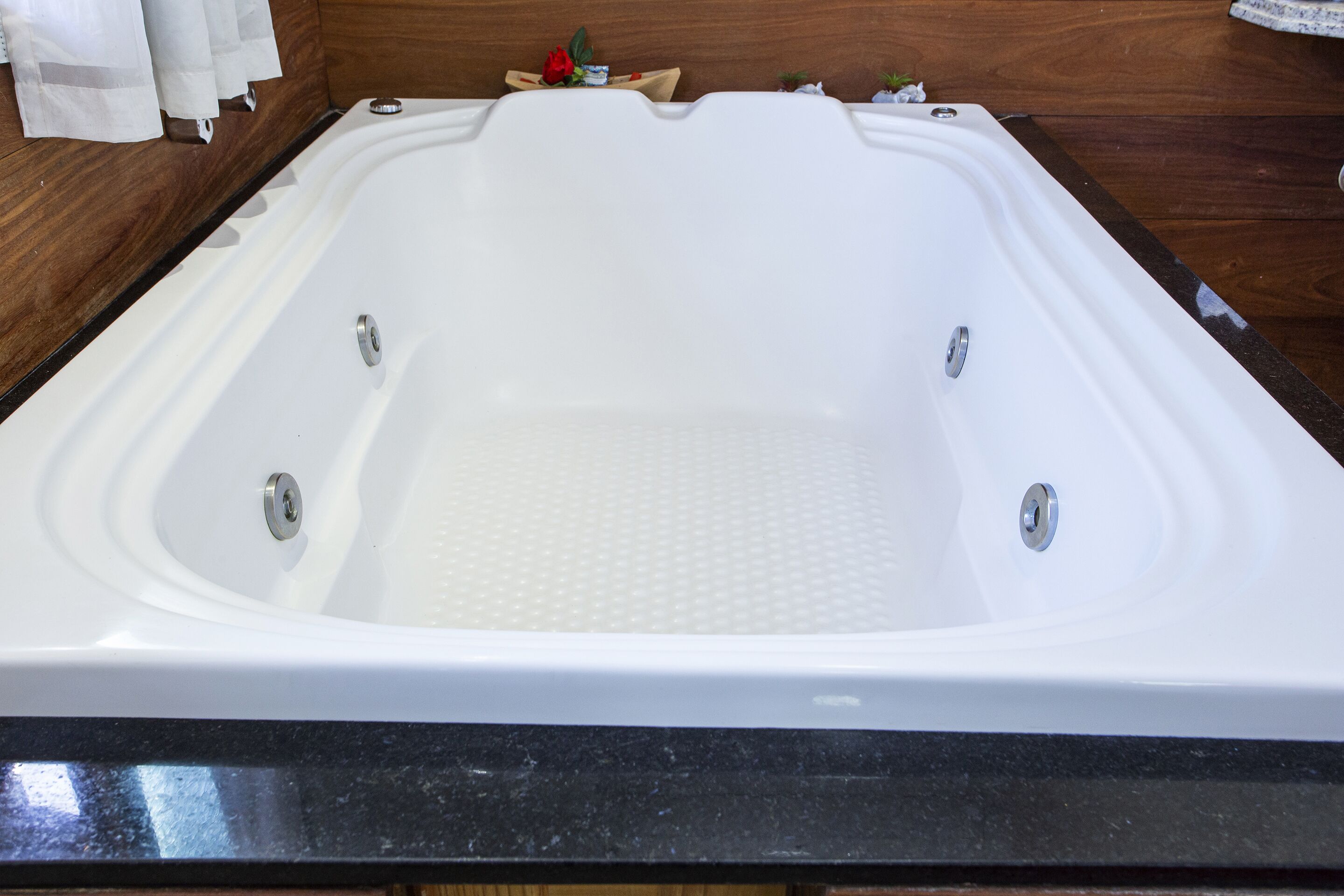 A large, rectangular hot tub with a textured bottom, set against a wooden wall and a black countertop.