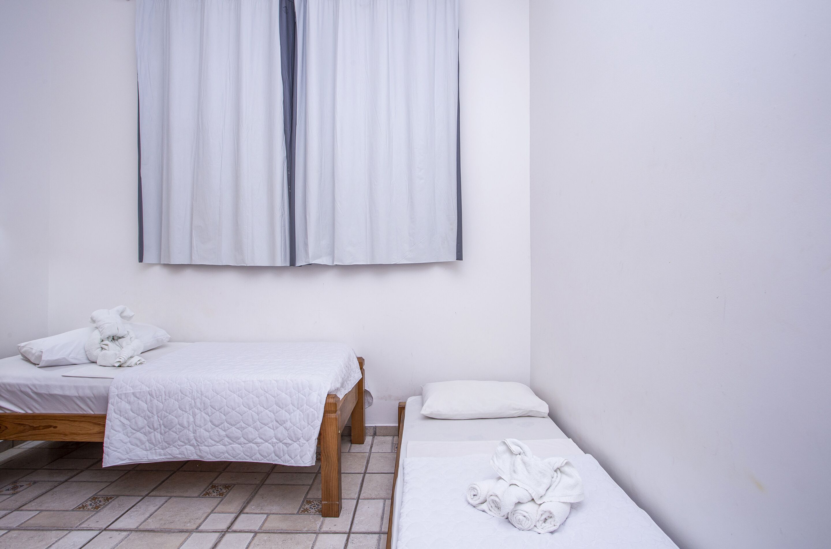 A small, clean room with two beds, a white curtain, and a tiled floor.