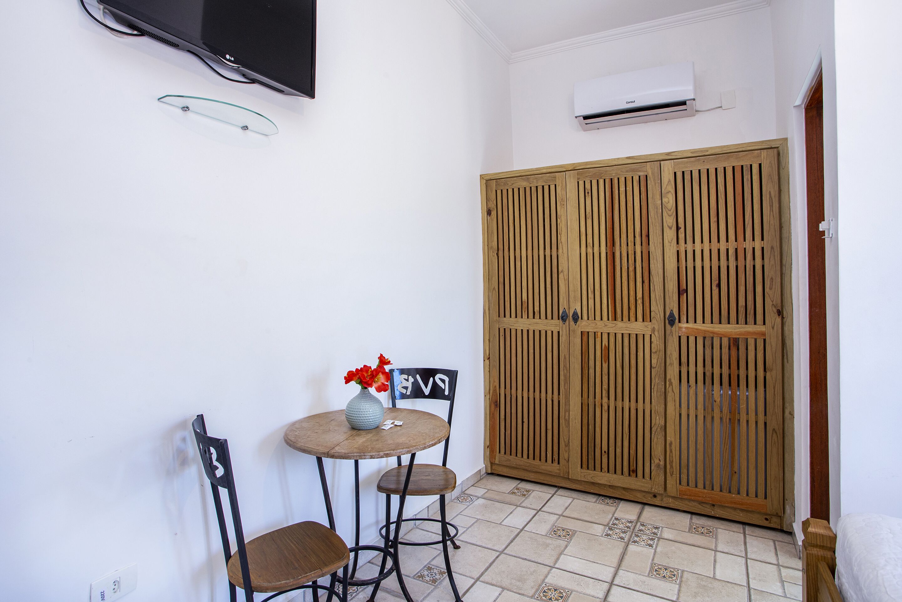 Una habitación pequeña con un armario de madera, una mesa redonda con dos sillas y un televisor montado en la pared.
