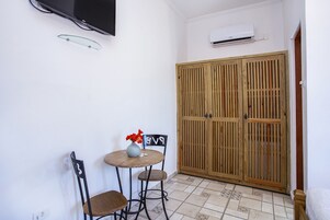 Una habitación pequeña con un armario de madera, una mesa redonda con dos sillas y un televisor montado en la pared.