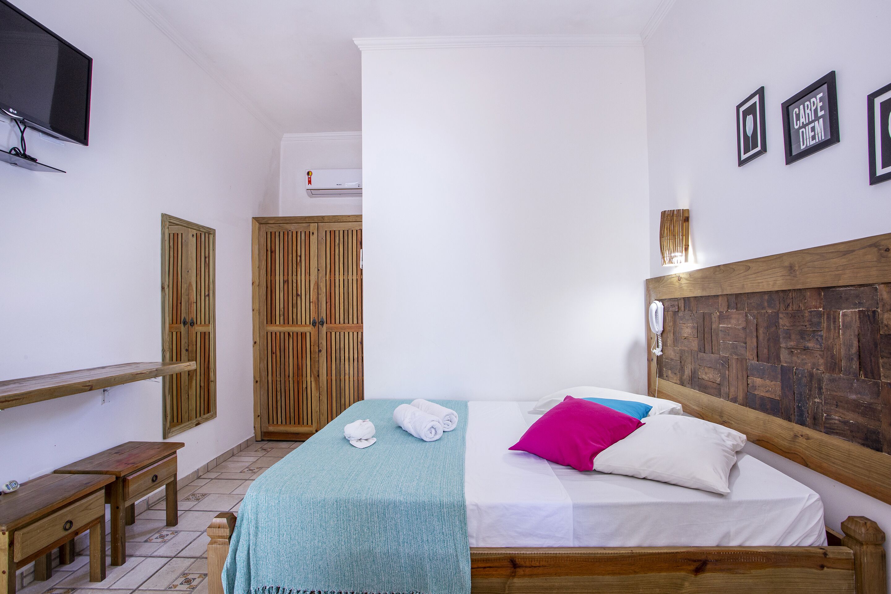Une chambre à coucher comprenant un lit, une tête de lit en bois, une table de chevet, un banc, une télévision et une armoire.