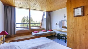 Une chambre avec un grand lit, une fenêtre avec des rideaux, un bureau avec une lampe et un tableau encadré au mur.