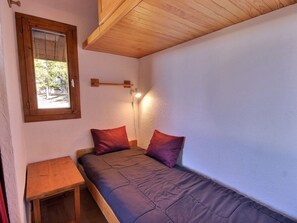 Une petite chambre avec un lit simple, un plafond en bois, une fenêtre donnant sur un paysage verdoyant et une table de chevet.