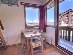 Une pièce avec une table et des chaises en bois, une fenêtre donnant sur les montagnes et un rideau rouge.