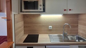 A compact kitchen with a built-in microwave, a stainless steel sink, and wooden cabinetry. - Studio for 4 in Vallandry, near slopes (Peisey-Vallandry)