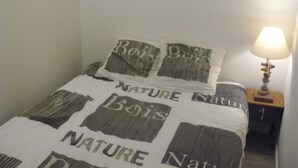 A bed with a nature-themed duvet cover and pillows, a bedside lamp, and a small wooden nightstand. - Nice T1 Bis ideally located, parking, wifi and garden (Thonon-les-Bains)
