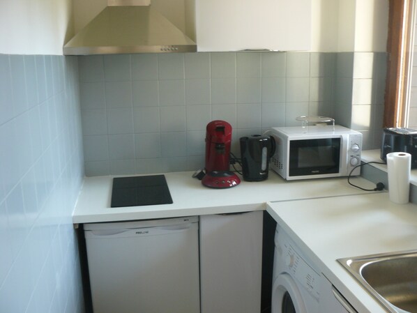 A compact kitchen with a dishwasher, a red coffee maker, a microwave, and a roll of paper towels.