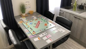 Ruokailutilassa on Monopoly-lautapeli, tuoleja ja pieni kasvi. Keittiöalueella on puolestaan pesuallas ja pullo.
