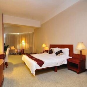 A hotel room with a large bed, two bedside tables with lamps, a desk, and a chair. - Plateau Pearl Hotel (Kunming)