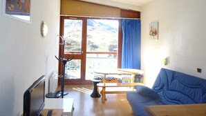 Un salon avec un canapé bleu, une table en bois et un balcon offrant une vue sur les montagnes.