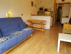 Un espacio habitable compacto con un sofá azul, una mesa de comedor de madera y una zona de kitchenette.