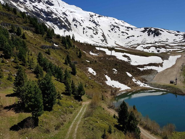 A mountainous landscape with a clear lake, a dirt path, and snow-capped peaks.