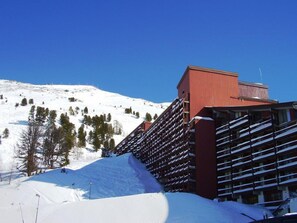 A hotel with a red facade, multiple balconies, and a snowy mountain backdrop.