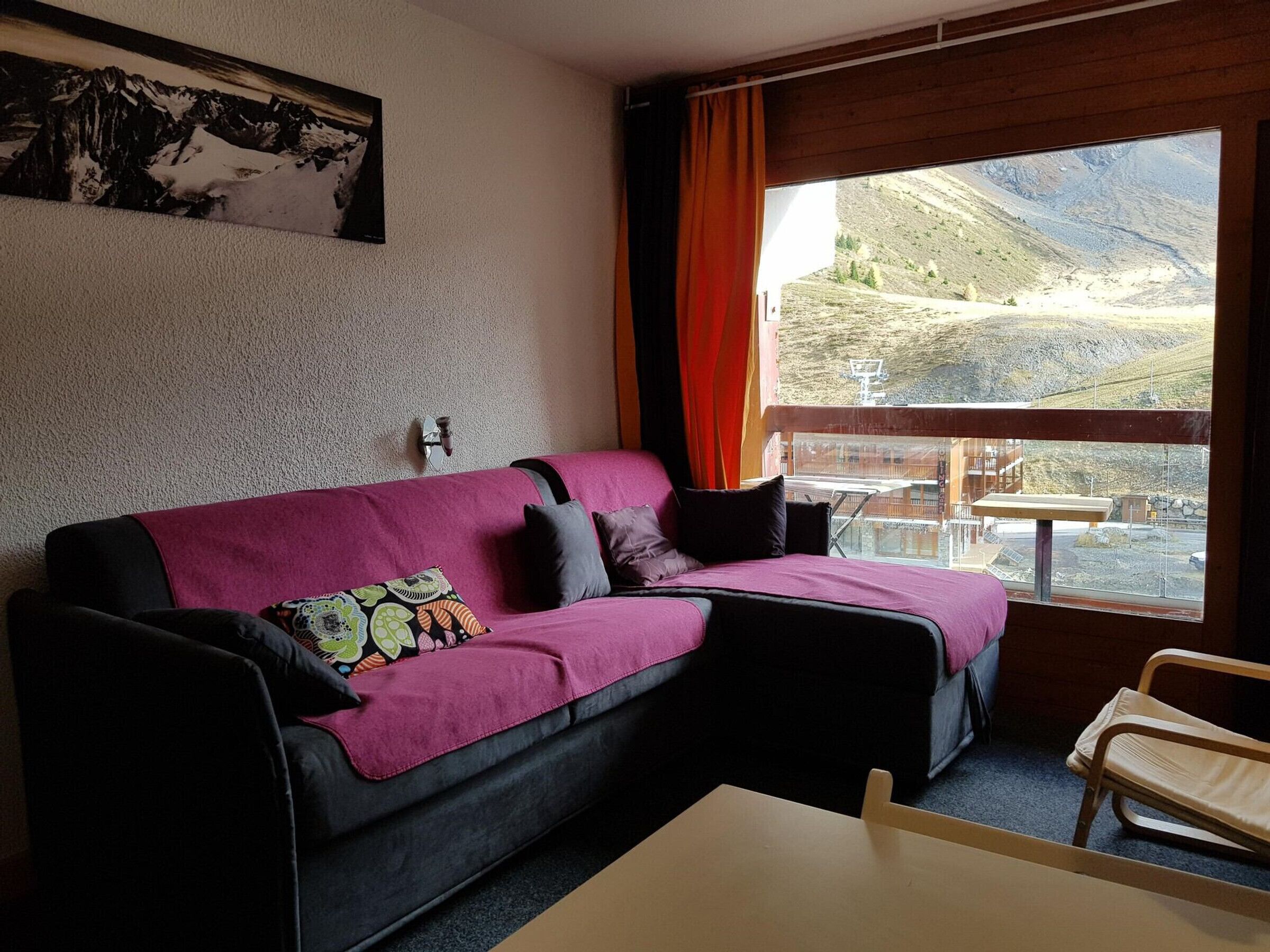 A room with a purple sofa, a small table, and a window with a view of a mountainous landscape.