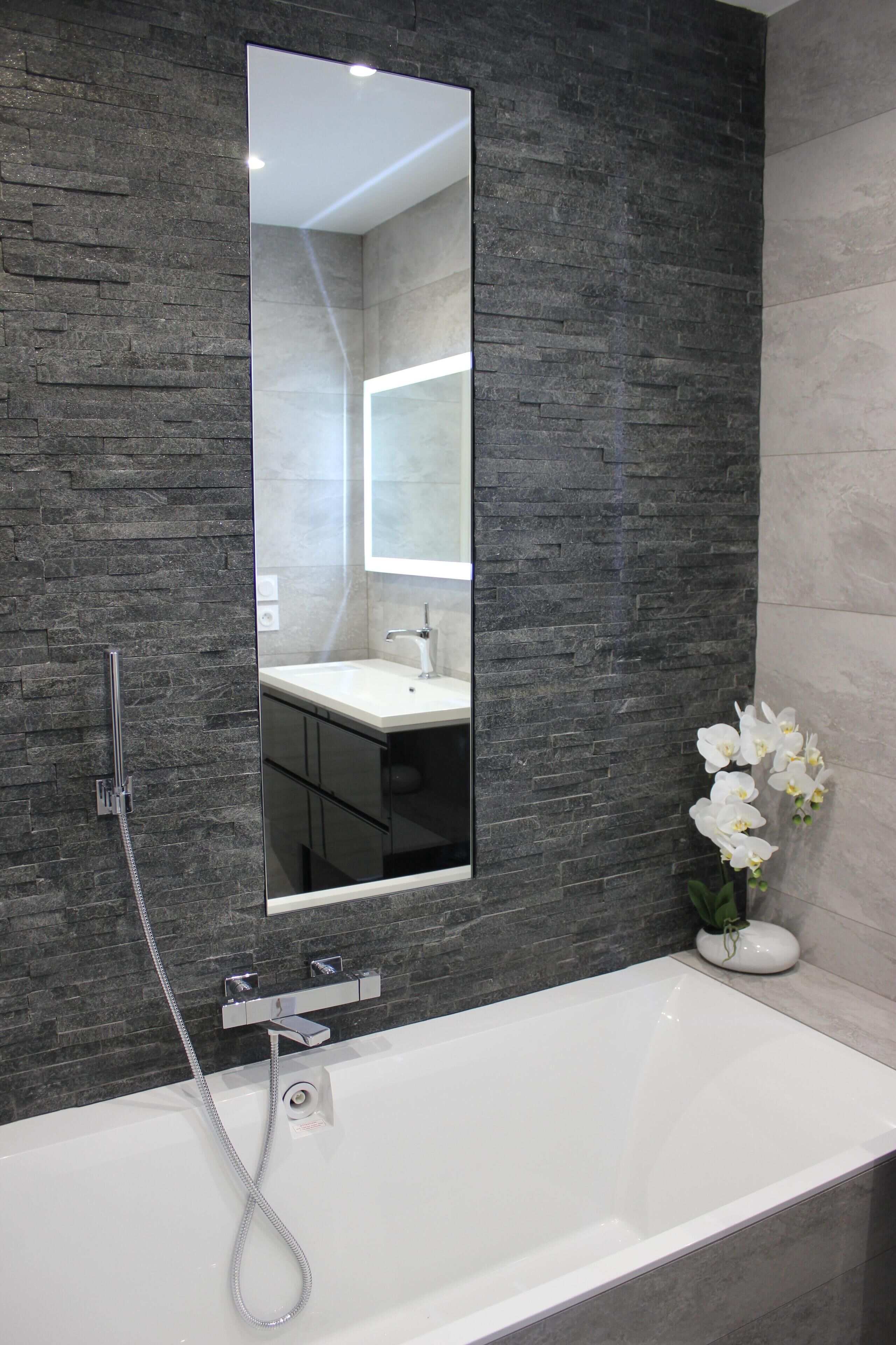 A modern bathroom with a large mirror, a white bathtub, and a shower.