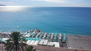 A beach with numerous umbrellas and sunbeds, a clear blue sea, and a distant shoreline.