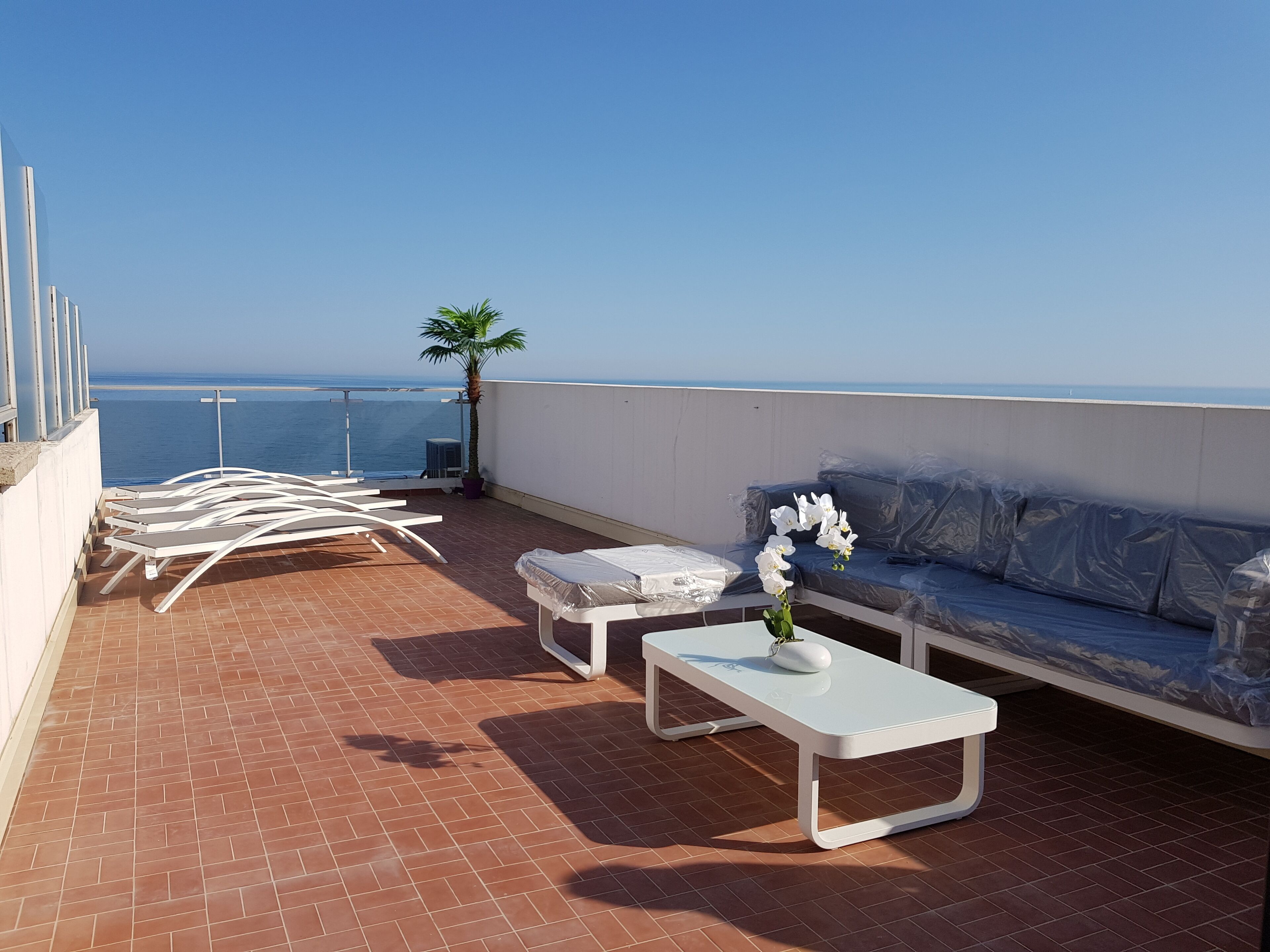 Een dakterras met witte lounge fauteuils, een witte tafel, een overdekte bank en een potplant.