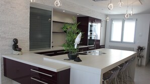 A modern kitchen with a central island, bar stools, and a potted plant. - 2 Bedroom Apartment 84m² Promenade des Anglais Last Floor sea View + Solarium (Nice)