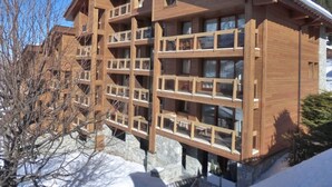 A multi-story wooden building with balconies, likely a hotel or lodge, surrounded by snow and trees.
