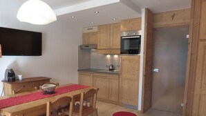 A compact kitchen with wooden cabinets, a built-in oven, and a dining area with a red table and chairs.