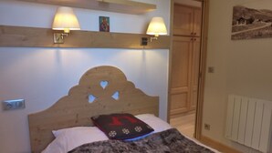 A bedroom with a wooden headboard, two wall-mounted lamps, a bed with a fur throw, and a door leading to another room.