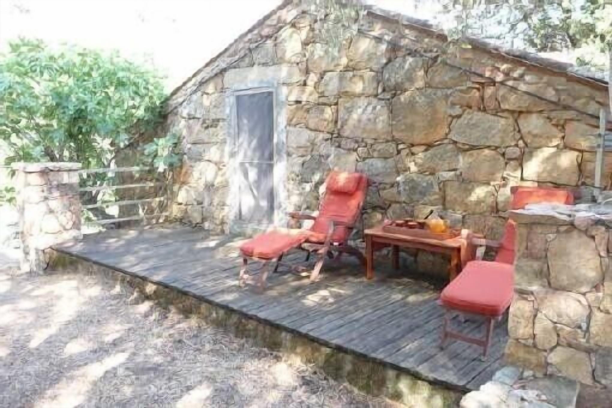 A stone building with a wooden deck, two red lounge chairs, and a small table with a bottle and glasses.