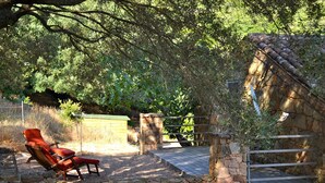 A stone-walled outdoor seating area with two red lounge chairs and a wooden deck. - Charming traditional home in the quiet groves. 10 minutes from beaches (Sartene)