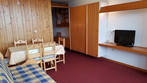 Una camera spaziosa con un letto, un tavolo da pranzo con sedie, una TV su uno scaffale e un armadio.