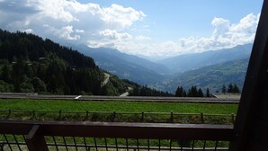 Una vista panoramica da un balcone con ringhiera metallica, su una valle con montagne e una strada.