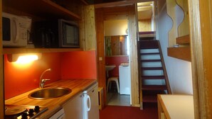Una cucina compatta con lavello, fornello e forno a microonde. Una scala in legno conduce a una zona pranzo.