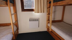 A dormitory room with bunk beds, a window with curtains, and a wall-mounted heater.