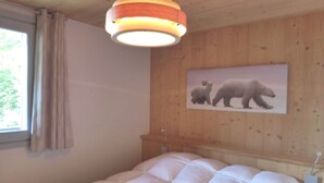 A bedroom with a large bed, a wooden headboard, a window with curtains, and a wall-mounted picture of polar bears. - Lovely apartment in Méribel center, close to slopes, for 5 persons (Méribel)