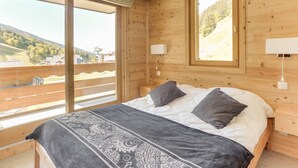 Un dormitorio de cabaña de madera con una cama grande, dos lámparas de noche y vista a un área boscosa a través de una ventana.