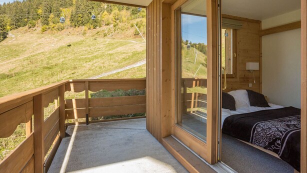 Una cabaña de madera con balcón que da a una ladera cubierta de hierba y un telesilla.