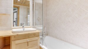 Un baño con tocador de madera, lavamanos blanco y cabina de ducha de vidrio.