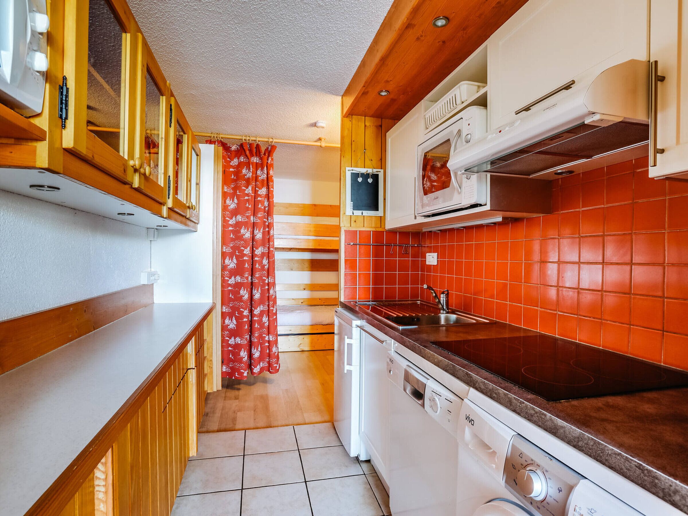 Eine kleine Küche mit Holzausstattung, einer Mikrowelle, einem Geschirrspüler und einer roten Fliesenrückwand.