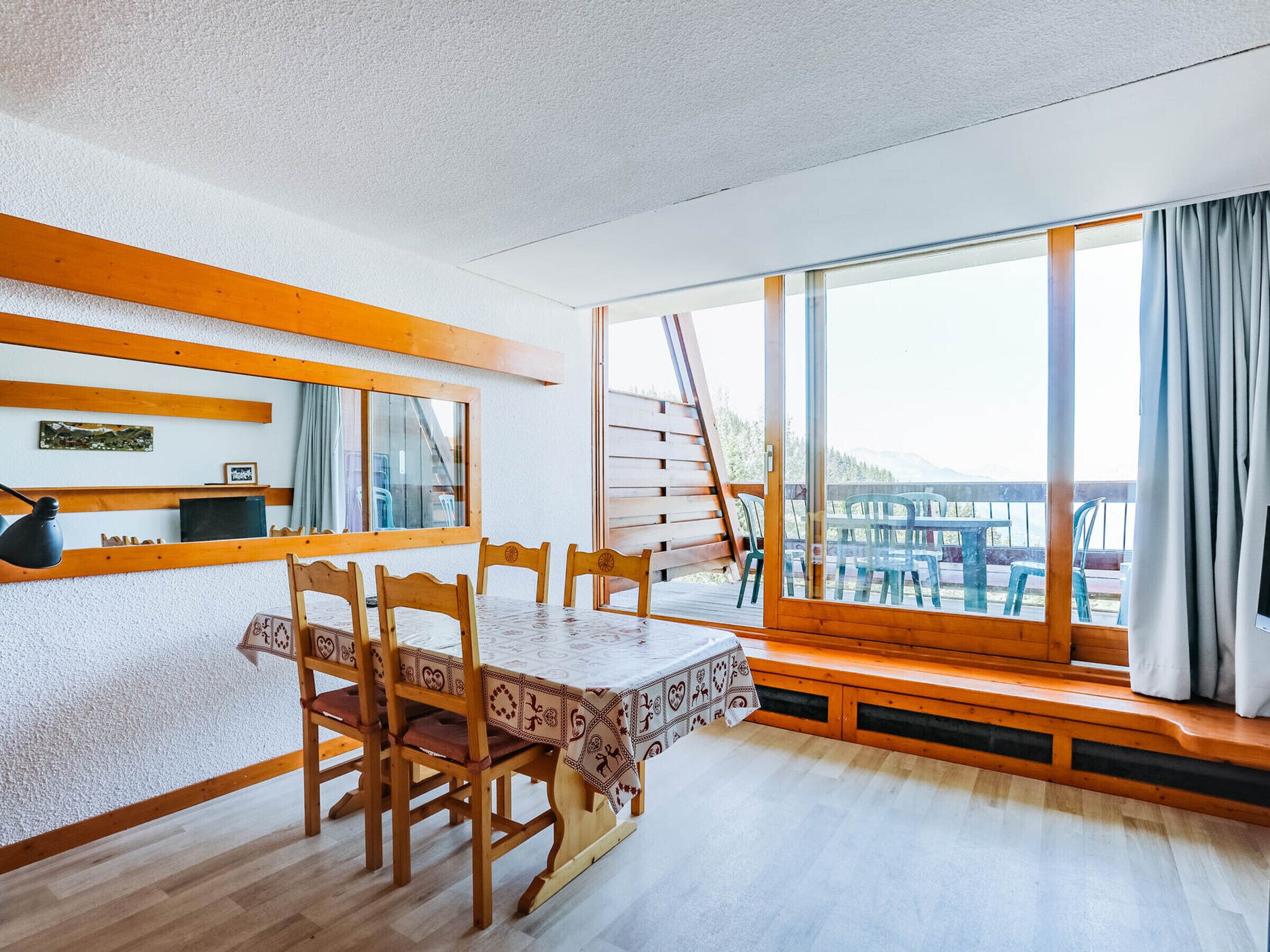 Un comedor con mesa y sillas de madera, un ventanal con vistas al exterior y un banco de madera junto a la ventana.