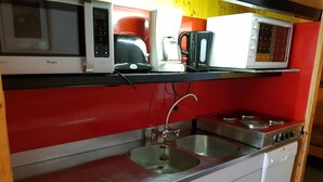 Eine kompakte Küche mit einer Mikrowelle, einer Kaffeemaschine und einem Toaster auf einer Ablage, einem Spülbecken mit Armatur und einem Herd.