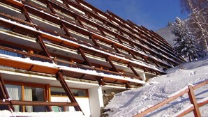 Ein mehrgeschossiges Gebäude mit geneigtem Dach, wahrscheinlich ein Hotel oder Resort, mit Blick auf einen verschneiten Berg im Hintergrund.
