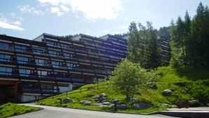 Ein modernes Gebäude mit flachem Dach und zahlreichen Fenstern, umgeben von Grünflächen und einer gepflasterten Fläche.
