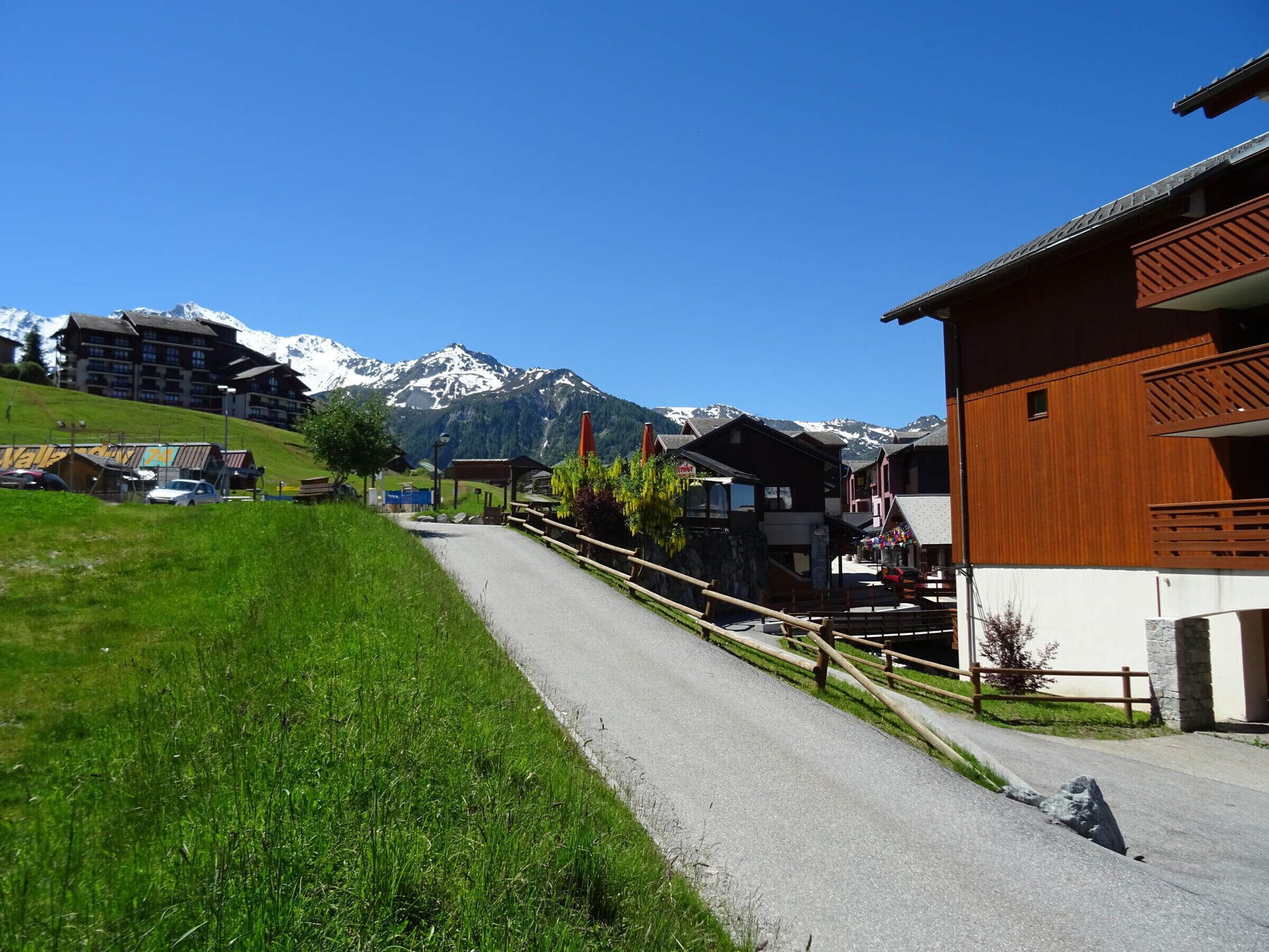 Un villaggio di montagna con case tradizionali in legno, una strada pavimentata e montagne innevate sullo sfondo.