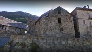 Um edifício de pedra com estilo arquitetônico tradicional, apresentando uma parede de pedra e uma pequena varanda no andar superior.