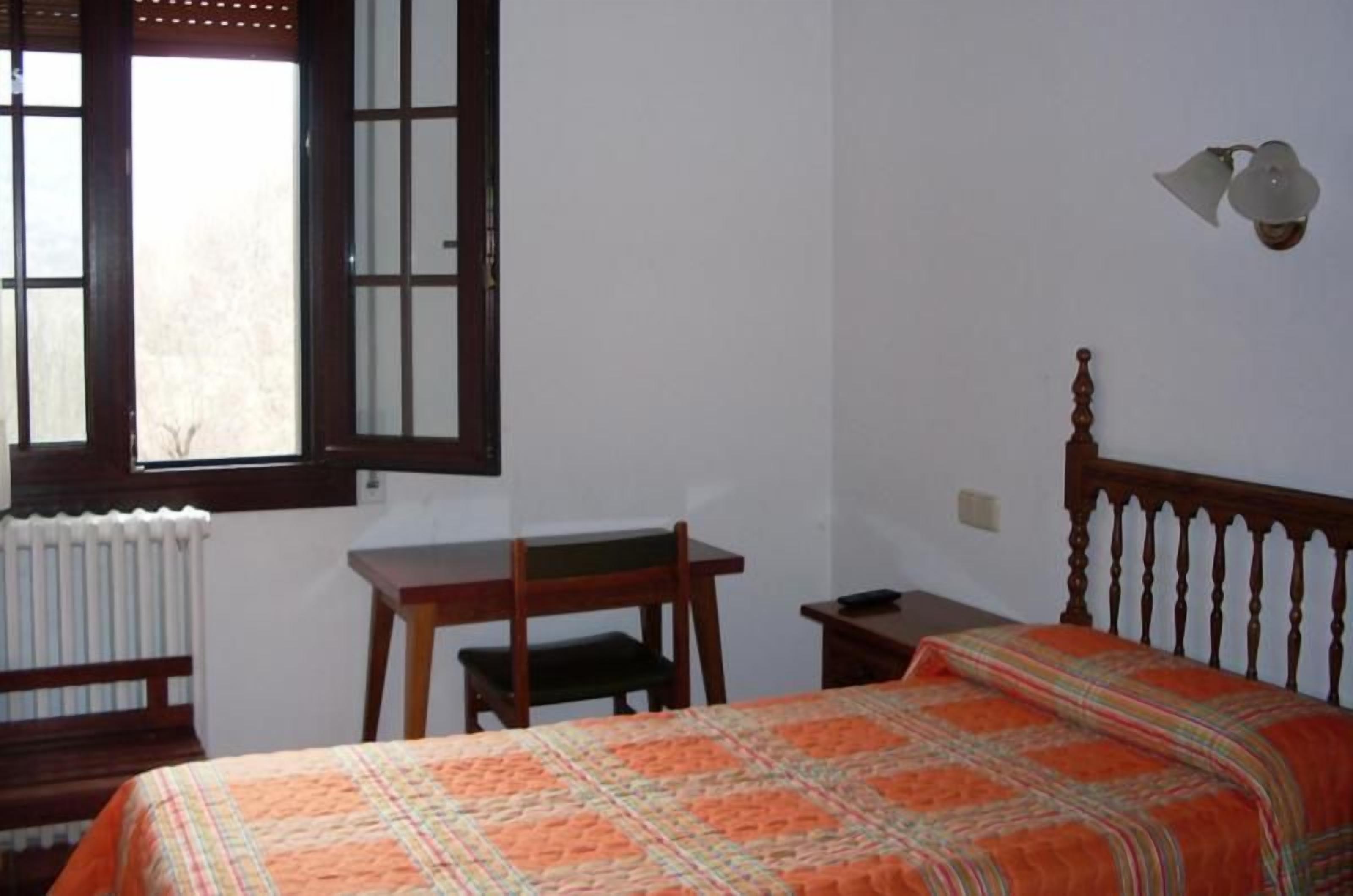Een slaapkamer met een bed, een bureau, een stoel, een radiator en een raam met uitzicht.