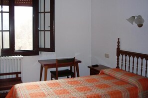 A bedroom with a bed, a desk, a chair, a radiator, and a window with a view.